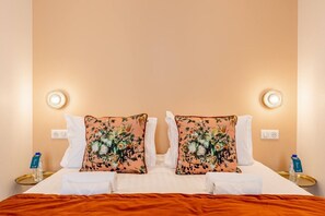 A hotel room with a bed, two pillows with floral designs, bedside tables with water bottles, and wall-mounted light fixtures. - B3D. 4 people—Champs-Élysées—Wagram—Arc de Triomphe—AC (Paris)