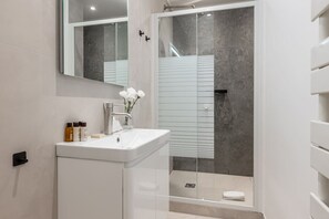 A modern bathroom with a white sink, a mirror, and a glass-enclosed shower. - B3D. 4 people—Champs-Élysées—Wagram—Arc de Triomphe—AC (Paris)
