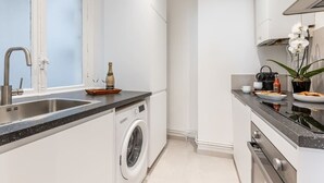 Une cuisine moderne équipée d’un lave-linge intégré, d’un évier et d’un plan de travail sur lequel se trouvent une bouteille de champagne et des verres.