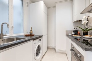 A modern kitchen with a built-in washing machine, a sink, and a countertop with a bottle of champagne and glasses. - B3D. 4 people—Champs-Élysées—Wagram—Arc de Triomphe—AC (Paris)