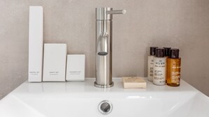 A bathroom sink with a modern faucet, a dental set, a vanity set, a shower cap, and a set of hair and body care products. - B6G - 2people - Wagram - Studio - Ternes - AC (Paris)