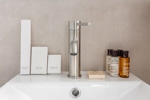 A bathroom sink with a modern faucet, a dental set, a vanity set, a shower cap, and a set of hair and body care products. - B6G - 2people - Wagram - Studio - Ternes - AC (Paris)