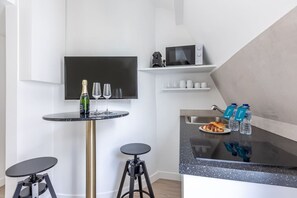 A modern kitchen with a black countertop, a wine bottle, and glasses on a small round table. - B6G - 2people - Wagram - Studio - Ternes - AC (Paris)