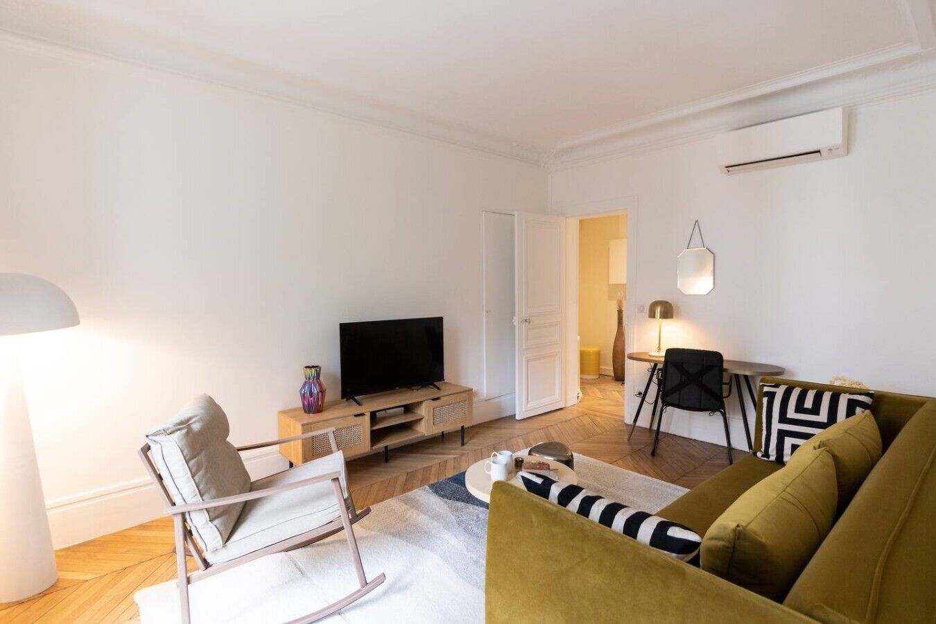 A modern living room with a flat-screen TV, a sofa, a chair, and a dining area with a table and chairs.