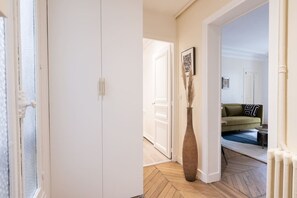 Ein Flur mit einer weißen Tür, einer Vase mit Pampasgras und einem grünen Sofa im Hintergrund.