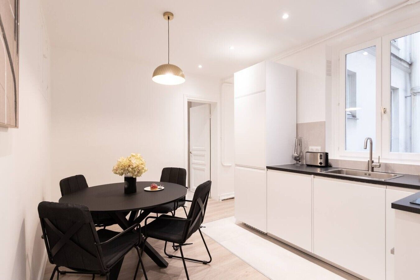 Een moderne keuken met witte kasten, een zwart aanrecht en een ronde eettafel met stoelen.