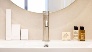 A bathroom with a sink, a mirror, and toiletries including a dental set, vanity set, shower cap, and Nuxe body care products. - B1G. 4 people—Champs-Élysées—Wagram—Arc de Triomphe—AC (Paris)