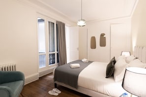 Ein Hotelzimmer mit Bett, Stuhl, einem fenster mit Vorhängen, Heizkörper und Lampe.