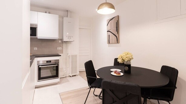 A modern kitchen with white cabinets, a built-in oven, and a dining area with a round table and black chairs. - B1G. 4 people—Champs-Élysées—Wagram—Arc de Triomphe—AC (Paris)