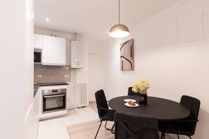A modern kitchen with white cabinets, a built-in oven, and a dining area with a round table and black chairs. - B1G. 4 people—Champs-Élysées—Wagram—Arc de Triomphe—AC (Paris)