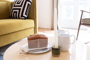 Ein Brot auf einem Teller mit einem Messer, einer Tasse und einer Kerze auf einem Tisch in einem Zimmer mit einer Couch und einem Fenster.