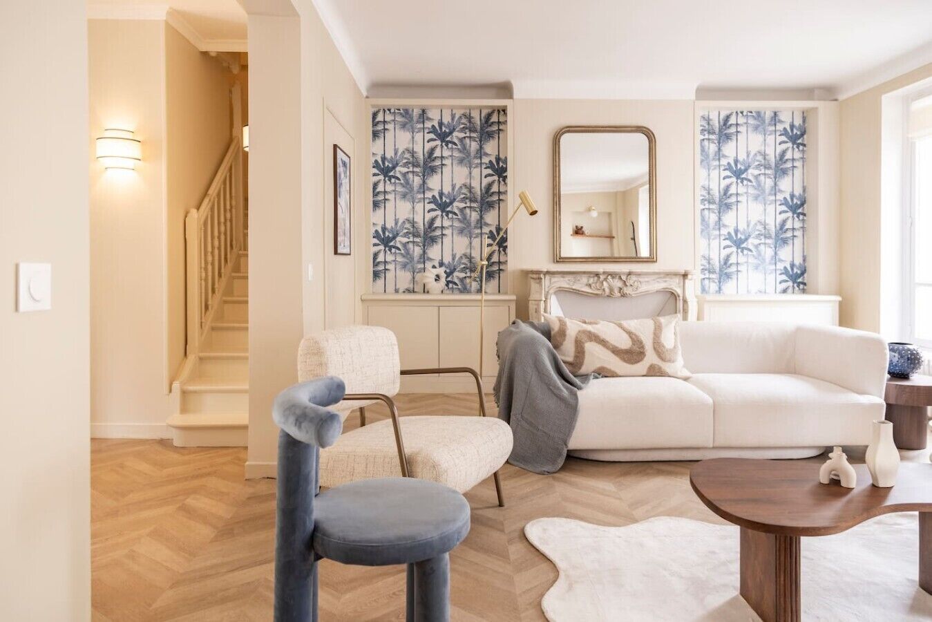 A living room with a white sofa, a blue chair, a wooden coffee table, and a patterned wall.