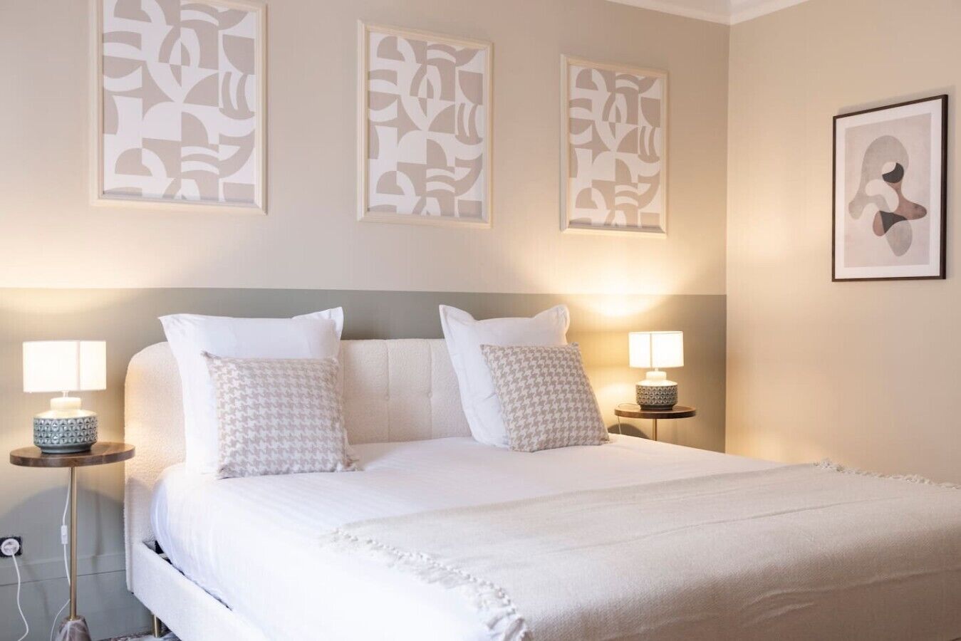 Une chambre d’hôtel avec un grand lit, deux lampes de chevet et trois œuvres d’art abstraites accrochées au mur.