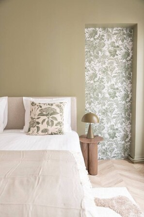 Ein Schlafzimmer mit einem Bett, einem Nachttisch und einer Wand mit floralem Wandpapier.