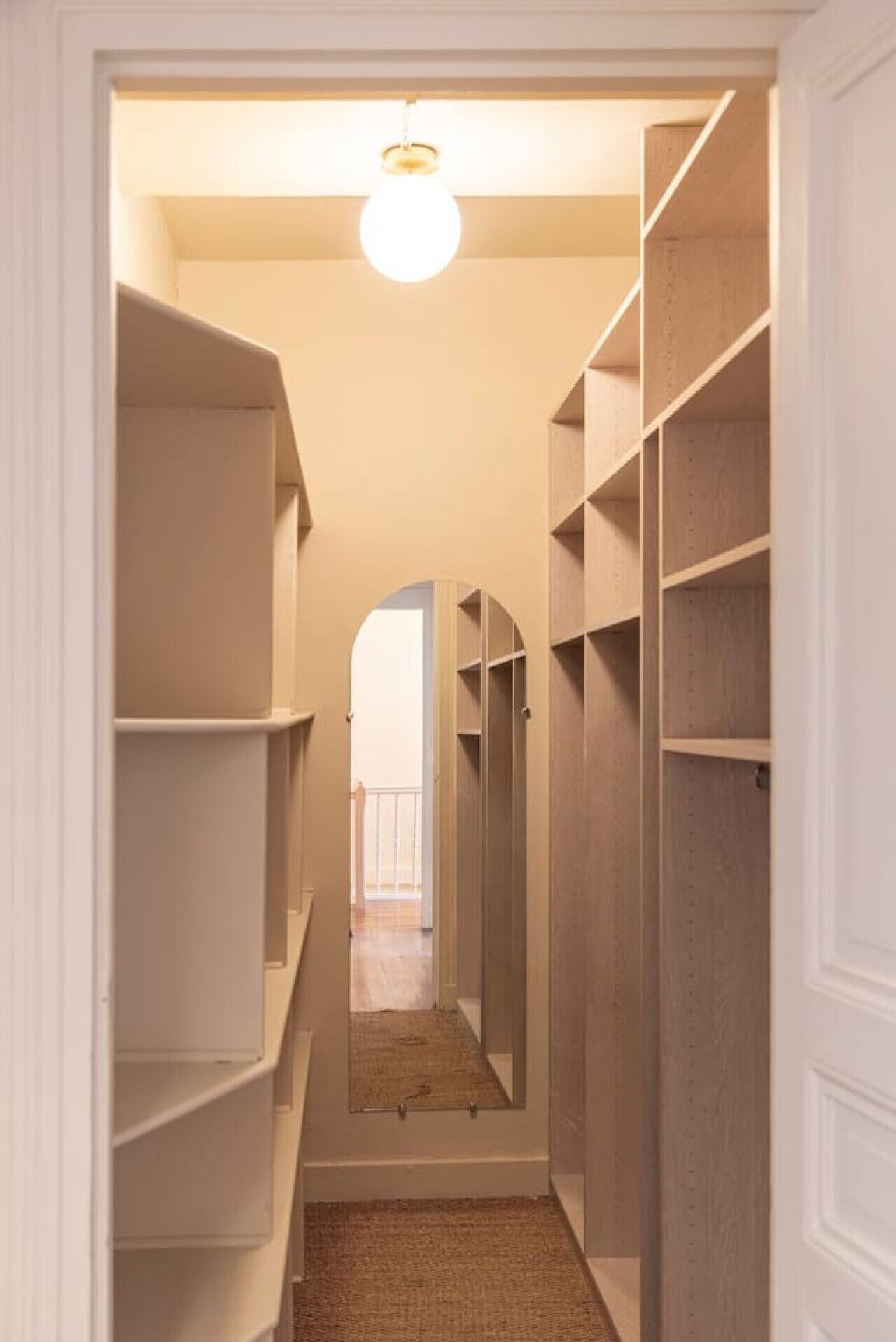 A narrow hallway with built-in shelving units on both sides, leading to a door at the end.