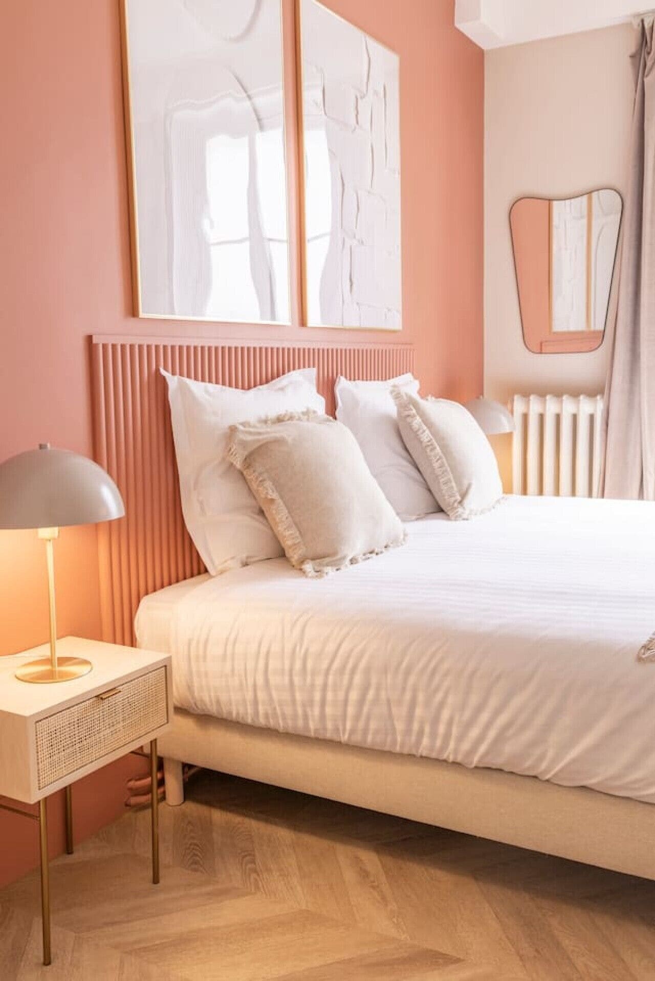 A bedroom with a bed, bedside table, lamp, and artwork on the wall.