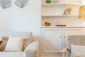 Ein Wohnzimmer mit einer Couch, Sesseln, einem Schrank und dekorativen Gegenständen auf Regalen.
