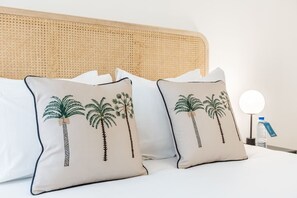 A bed with two pillows featuring palm tree designs, a round bedside table with a water bottle, and a wall-mounted lamp. - B2D-2 people-Wagram-1 bedroom-Ternes-AC (Paris)