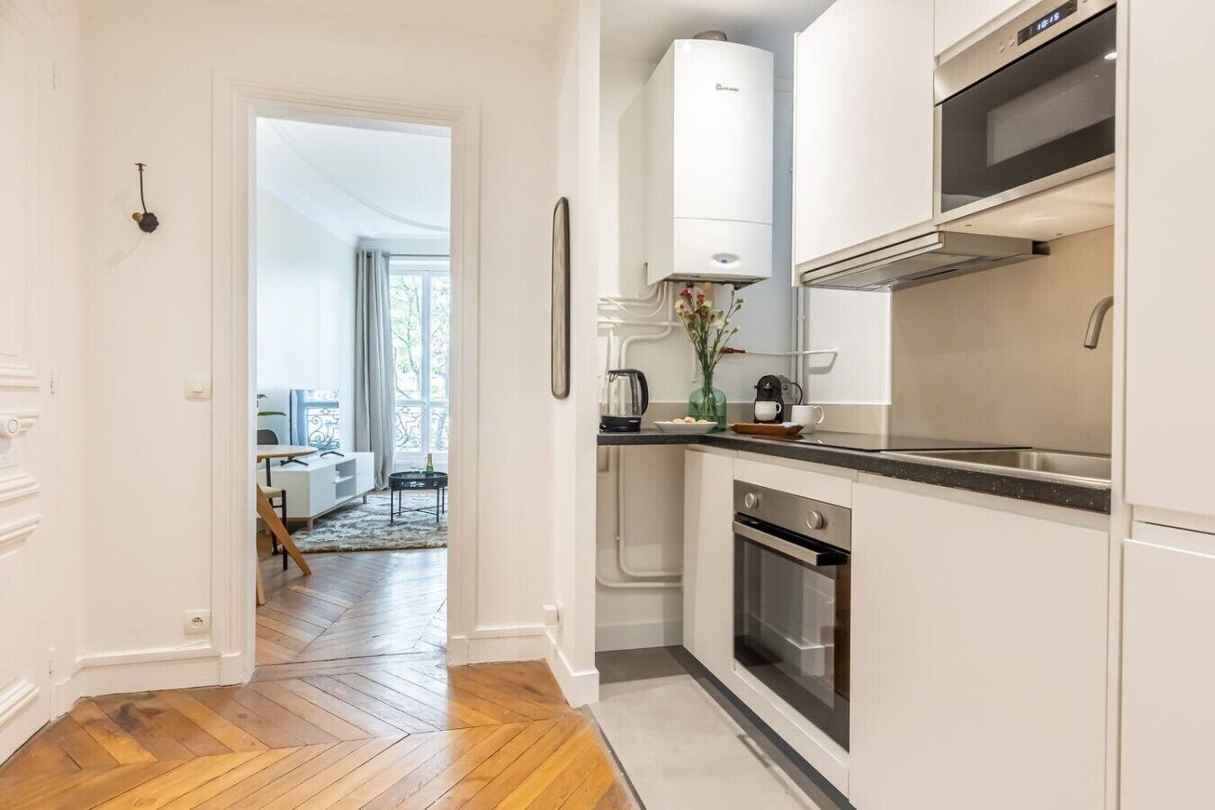 A modern kitchen with white cabinetry, a built-in oven, and a stainless steel range hood.