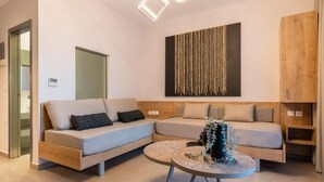 A modern living room with a sectional sofa, a round coffee table, and a wall-mounted artwork. - SARTI PREMIUM LUXURY SUITES  (SITHONIA)