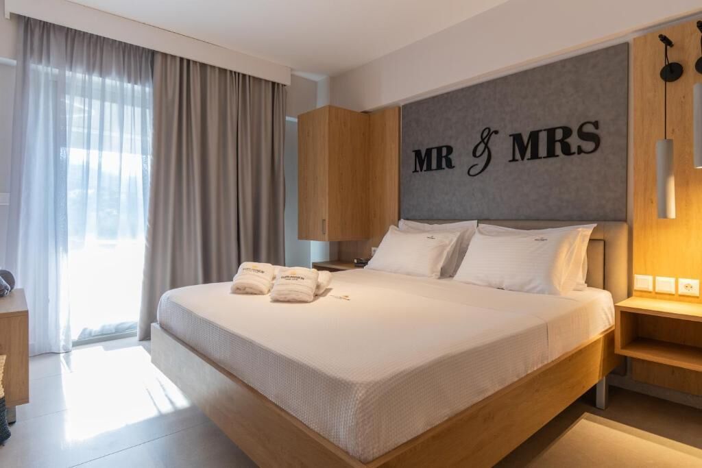 A hotel room with a large bed, a headboard with 'MR & MRS' lettering, a wooden wardrobe, and a bedside table with a lamp.