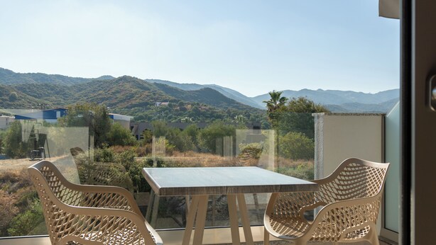 A balcony with a table and chairs, offering a view of a mountainous landscape. - SARTI PREMIUM LUXURY SUITES  (SITHONIA)