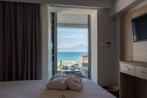 Une chambre d’hôtel équipée d’un lit, d’une télévision, d’un bureau et offrant une vue sur la mer et les montagnes.