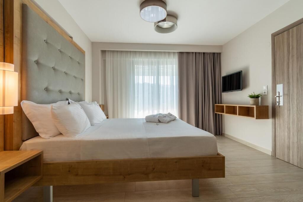 A modern bedroom with a large bed, a headboard, a bedside table, a TV, and a window with curtains.