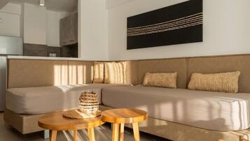 Una sala de estar moderna con un sofá, dos mesitas de madera y un cuadro abstracto negro en la pared.