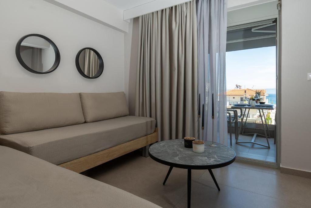 En moderne stue med en sofa, to vægmirror, et rundt sofabord og udsigt til en balkon med udendørs møbler.