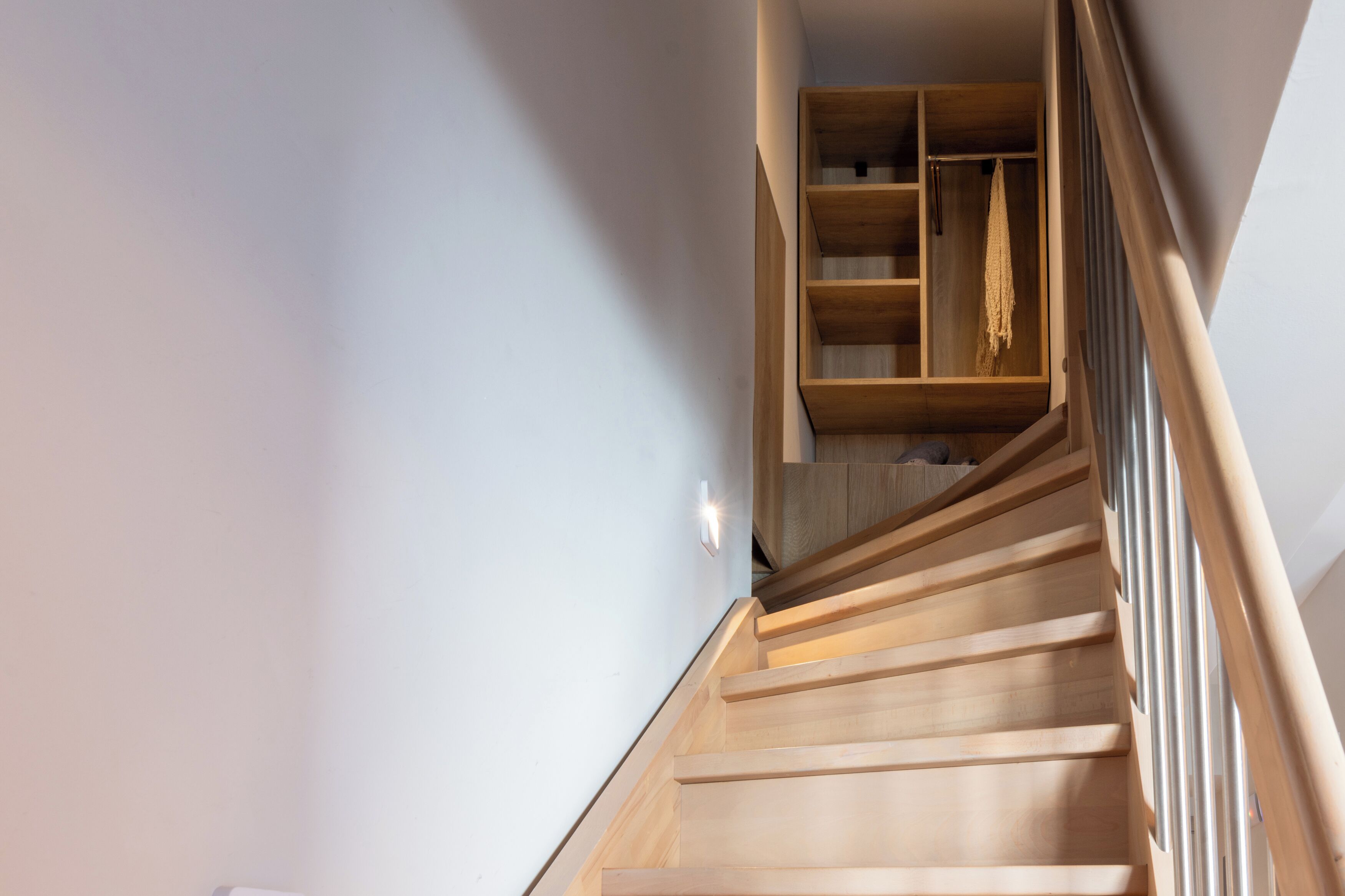Una scala in legno con ringhiera che conduce a una stanza con pavimento in legno e parete bianca.