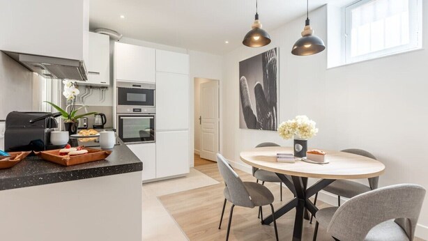 Una cocina moderna con comedor, que incluye una isla central, luces colgantes y vista del comedor contiguo.