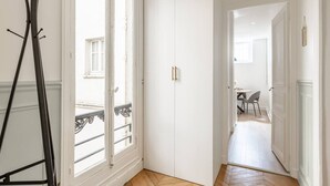 Un pasillo con un armario blanco, una puerta que da a un balcón y una zona de comedor con sillas y una mesa.