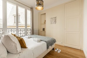 A bedroom with a bed, a radiator, a door, and a window with a view of buildings. - B3G. 4 people—Champs-Élysées—Wagram—Arc de Triomphe—AC (Paris)