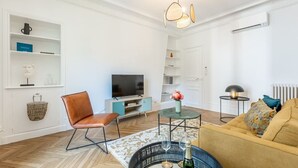 Una sala de estar moderna con una televisión, un sillón de cuero marrón, una mesa de centro redonda con copas de vino y un sofá con un plaid estampado.