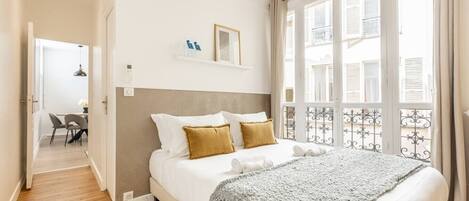 A bedroom with a bed, a bedside table, a window with a view, and a door leading to a balcony.
