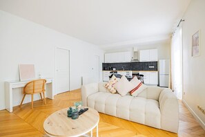 A modern living room with a sofa, a round coffee table, and a dining area with a chair and a small table. - Heart of Paris, 2-Bedroom Apartment, Arts et Métiers, Marais (Paris)