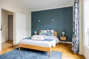 A bedroom with a bed, bedside tables, a blue rug, and a window with curtains. - Heart of Paris, 2-Bedroom Apartment, Arts et Métiers, Marais (Paris)