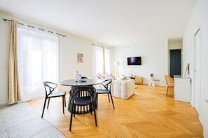 A modern living room with a round dining table, black chairs, a white sofa, and a flat-screen TV mounted on the wall. - Heart of Paris, 2-Bedroom Apartment, Arts et Métiers, Marais (Paris)