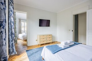 A hotel room with a bed, a television, a wooden dresser, and a view of the outside. - Heart of Paris, 2-Bedroom Apartment, Arts et Métiers, Marais (Paris)