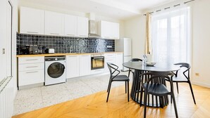 A modern kitchen with white cabinets, a dishwasher, an oven, and a dining area with a round table and chairs. - Heart of Paris, 2-Bedroom Apartment, Arts et Métiers, Marais (Paris)