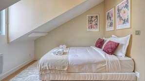 A bedroom with a sloped ceiling, a bed with white bedding and pink pillows, a white throw blanket, and two framed floral artworks on the wall. - 4G. 3-Bedroom Apartment for 6 People, Paris 15th Arrondissement, AC (Paris)