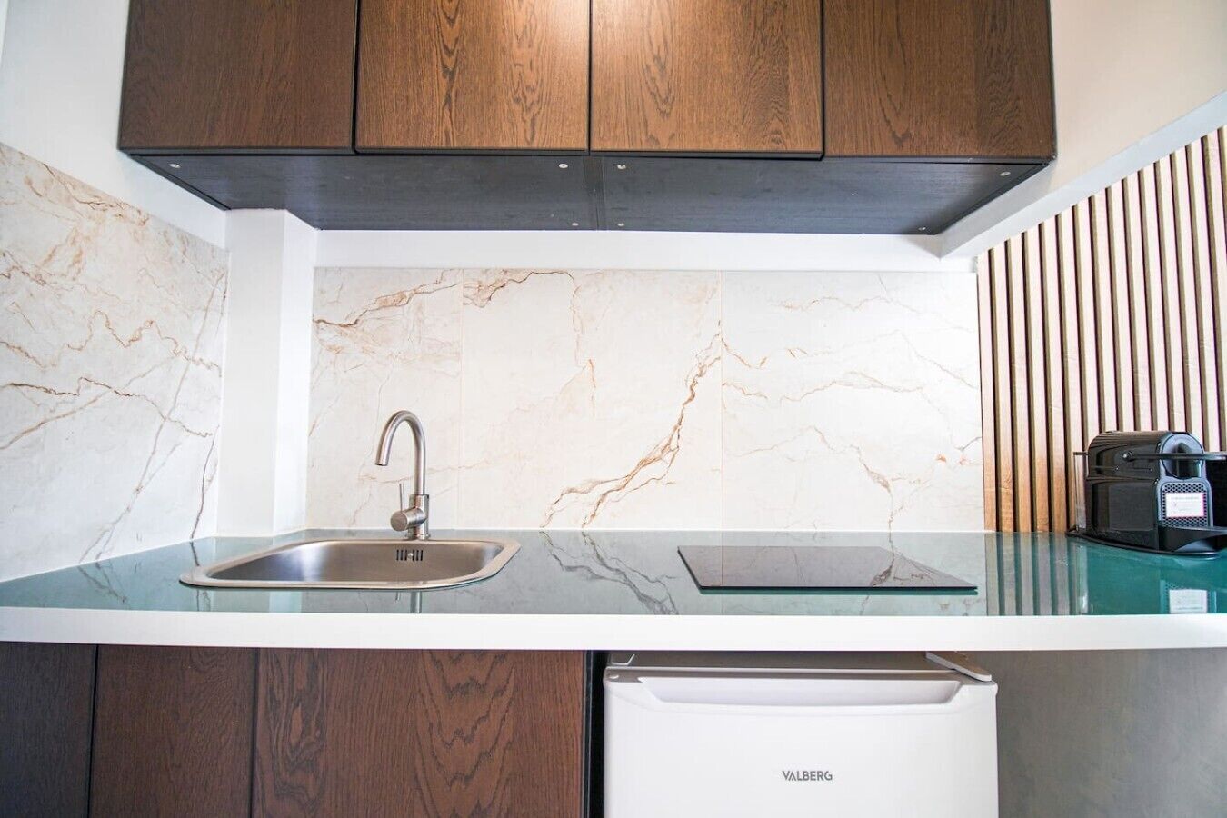 A kitchen with a marble backsplash, a stainless steel sink, wooden cabinets, and a built-in dishwasher.