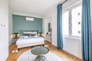 A hotel room with a bed, a round glass table, a window with curtains, and a mirror on the wall. - A4.Premium-Arc de Triomphe-Champs-Élysées-3 Bedrooms (Paris)