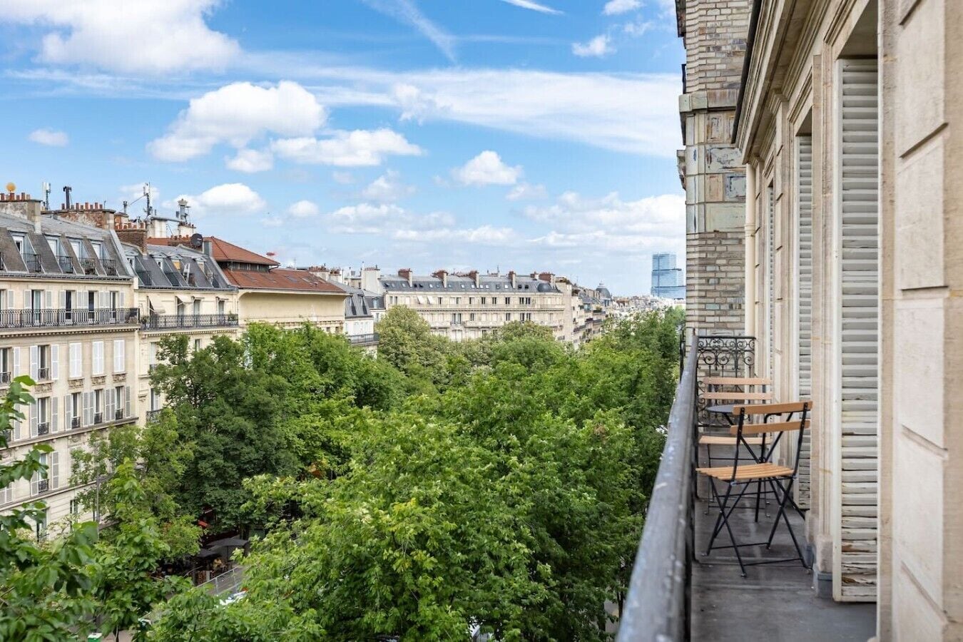 A balcony with a view of a cityscape, including buildings and trees.