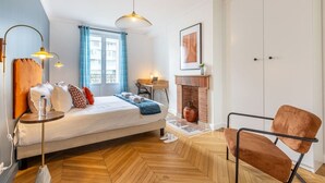 A bedroom with a bed, a desk, a chair, a fireplace, and a window with curtains. - A4.Premium-Arc de Triomphe-Champs-Élysées-3 Bedrooms (Paris)