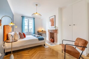 Quarto com cama, escrivaninha, cadeira, lareira e janela com cortinas.