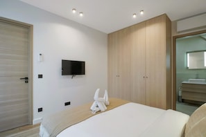 Ein Hotelzimmer mit Bett, Wandfernseher, Kleiderschrank und Badezimmer mit Spiegel und Waschbecken.