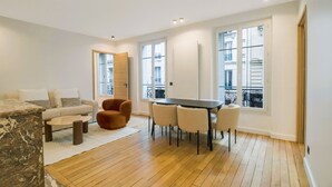 A modern living room with a sofa, a coffee table, a dining table with chairs, and a large window with a view of the city. - Premium Suites - Arc de Triomphe - Trocadéro (Paris)