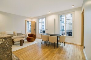 A modern living room with a sofa, a coffee table, a dining table with chairs, and a large window with a view of the city. - Premium Suites - Arc de Triomphe - Trocadéro (Paris)